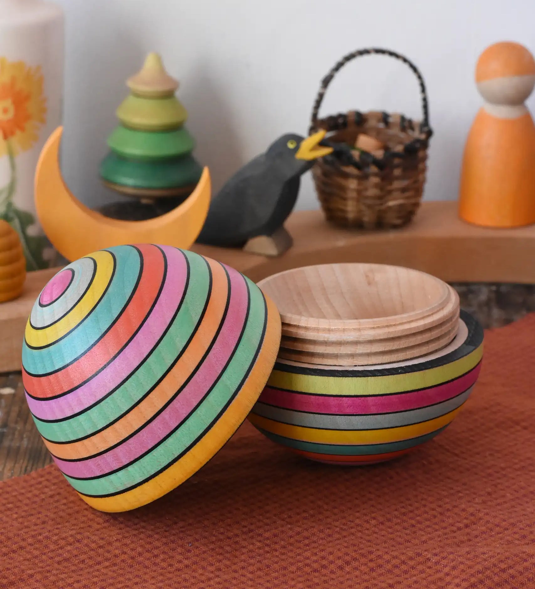Mader Kreiselmanufaktur roly-poly wooden egg in Spring opened and placed on a wooden surface in the Babipur playroom. The wooden thread can be seen on the sides of the egg.
