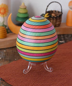 Mader Kreiselmanufaktur roly-poly wooden egg in Spring stripe colours placed on the clear display stand in the Babipur playroom.