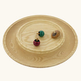 Mader Kreiselmanufaktur Rondell Ash Wood 40cm Spinning Plate with three wooden spinning tops placed on it.
