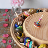Mader Kreiselmanufaktur 40cm Rondell Ash Wood Spinning Plate placed on a wooden surface in the Babipur playroom. Monalotte spinning top placed on the top with other spinning tops filling bottom part of the plate. 