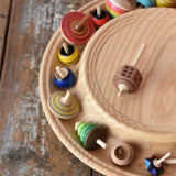 Mader Kreiselmanufaktur 40cm Rondell Ash Wood Spinning Plate placed on a wooden surface in the Babipur playroom. Dice spinning top placed on the top with other spinning tops filling bottom part of the plate. 