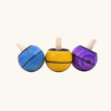 Three Mader Kreiselmanufaktur round ash turn over spinning top toys in various colours. Blue, yellow and purple.