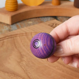 View of top of the Mader Kreiselmanufaktur round ash turn over spinning top toy in an adult's hand.