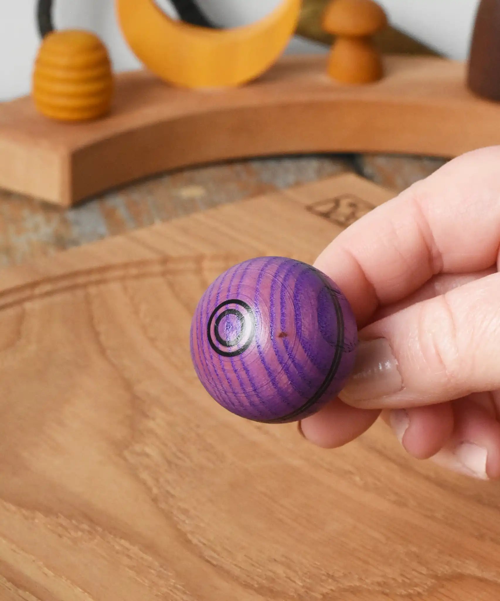 View of top of the Mader Kreiselmanufaktur round ash turn over spinning top toy in an adult's hand.