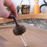 Mader Kreiselmanufaktur Salto Totale Walnut / Hornbeam Spinning Top placed on a walnut wood spinning plate in the Babipur playroom. Adult hand holding the top upright.