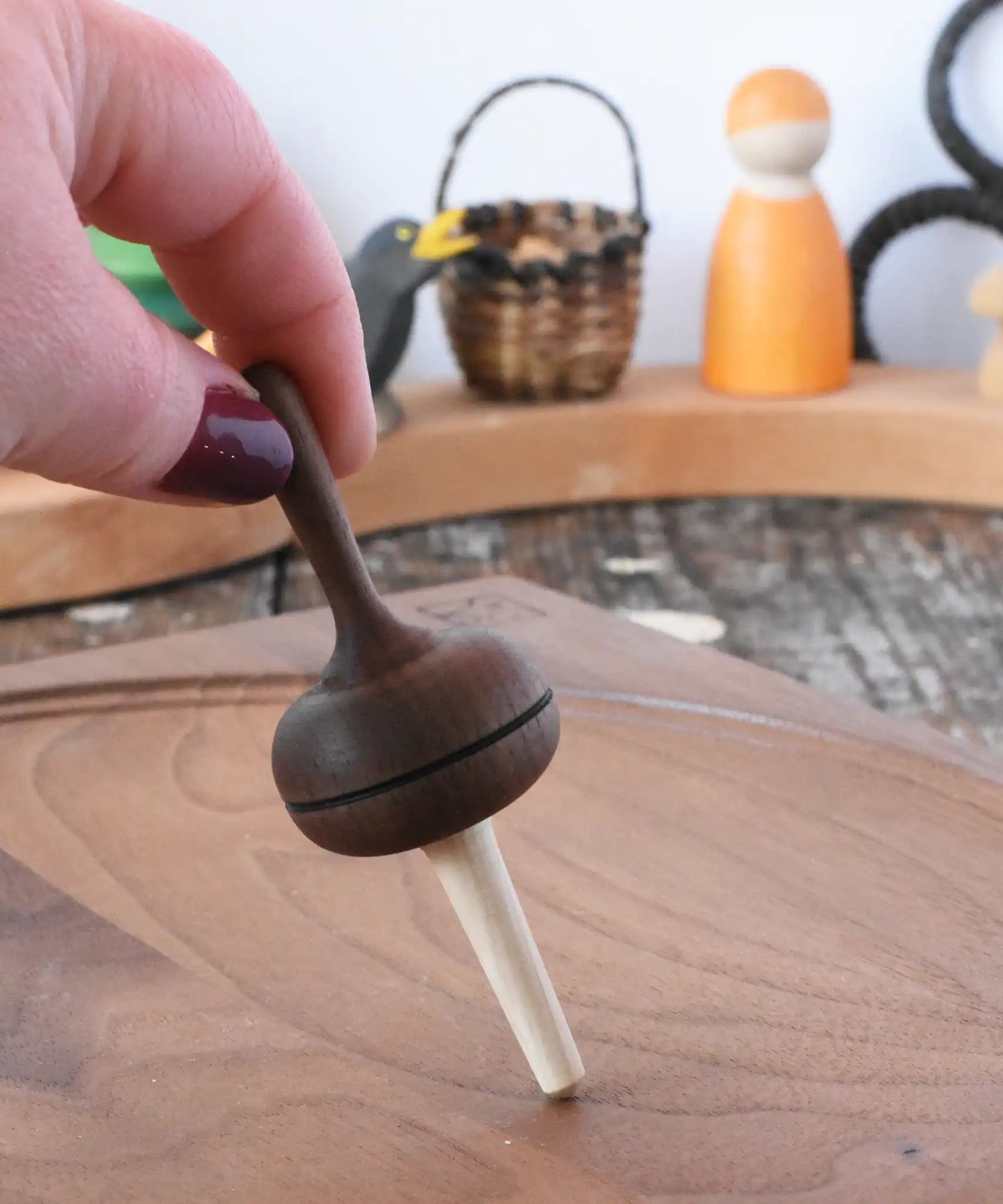 Mader Kreiselmanufaktur Salto Totale Walnut / Hornbeam Spinning Top placed on a walnut wood spinning plate in the Babipur playroom. Adult hand holding the top upright.