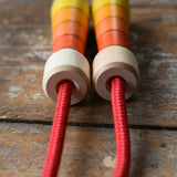 Close up of the top of the handles on the Mader Kreiselmanufaktur Children's Skipping Rope with Orange Handles placed on a wooden surface in the Babipur playroom. 
