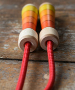 Close up of the top of the handles on the Mader Kreiselmanufaktur Children's Skipping Rope with Orange Handles placed on a wooden surface in the Babipur playroom. 
