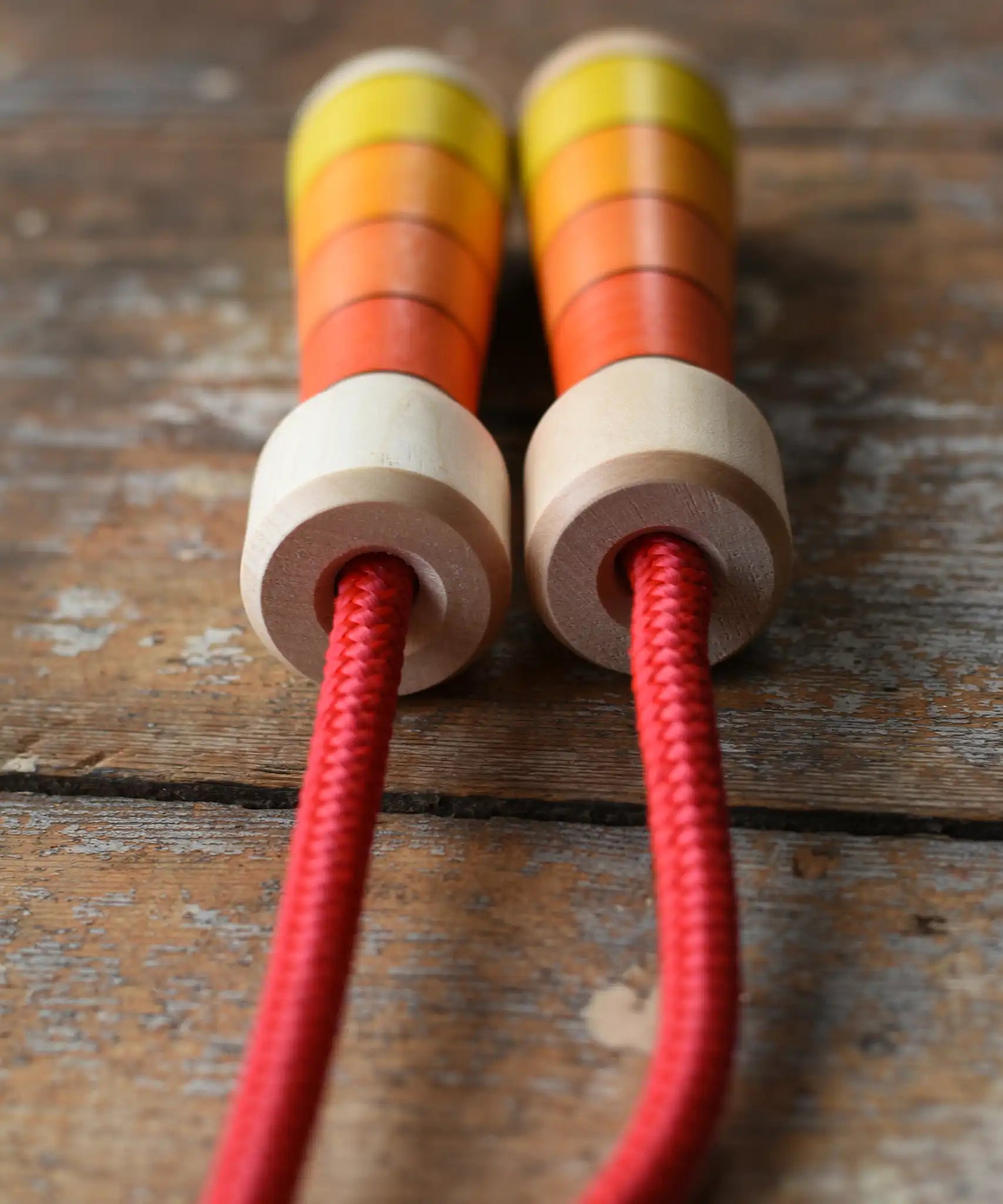 Close up of the top of the handles on the Mader Kreiselmanufaktur Children's Skipping Rope with Orange Handles placed on a wooden surface in the Babipur playroom. 
