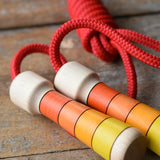 Close up view of the Mader Kreiselmanufaktur Children's Skipping Rope with Orange Handles placed on a wooden surface in the Babipur playroom. 