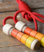 Close up view of the Mader Kreiselmanufaktur Children's Skipping Rope with Orange Handles placed on a wooden surface in the Babipur playroom. 