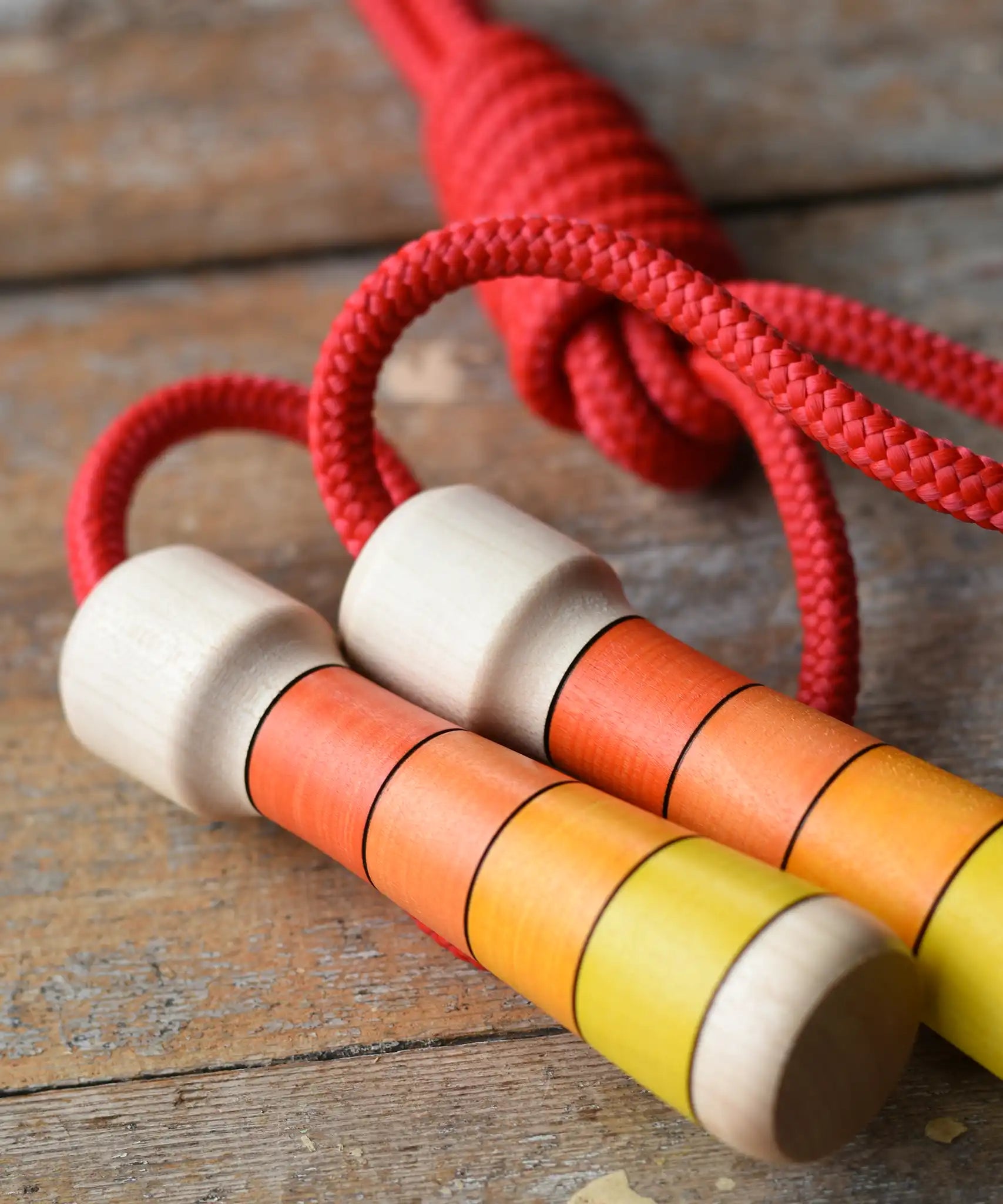 Close up view of the Mader Kreiselmanufaktur Children's Skipping Rope with Orange Handles placed on a wooden surface in the Babipur playroom. 