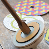 Mader 'So And So' DIY Spinning Top Set placed on a wooden desk in the Babipur playroom. Close up of square shaped base.