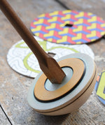 Mader 'So And So' DIY Spinning Top Set placed on a wooden desk in the Babipur playroom. Close up of square shaped base.