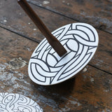 Mader 'So And So' DIY Spinning Top Set placed on a wooden desk in the Babipur playroom. The spinning to with one of the monochrome patterned discs placed on top. 