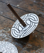 Mader 'So And So' DIY Spinning Top Set placed on a wooden desk in the Babipur playroom. The spinning to with one of the monochrome patterned discs placed on top. 