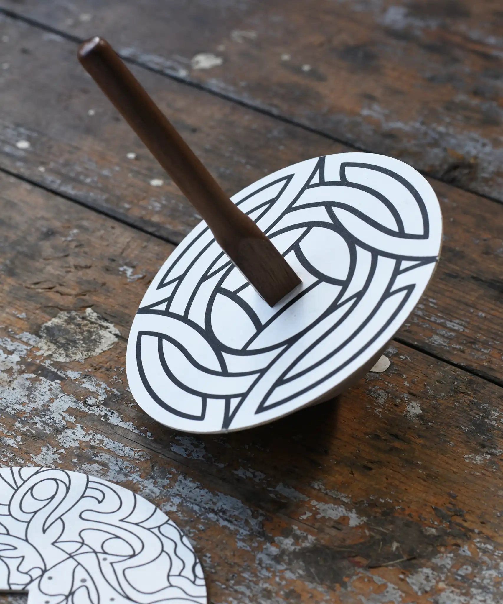 Mader 'So And So' DIY Spinning Top Set placed on a wooden desk in the Babipur playroom. The spinning to with one of the monochrome patterned discs placed on top. 
