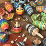 Collection of Mader spinning top learning sets in different colour variations all laid out on a wooden surface in the Babipur playroom. 
