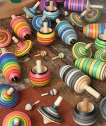 Collection of Mader spinning top learning sets in different colour variations all laid out on a wooden surface in the Babipur playroom. 