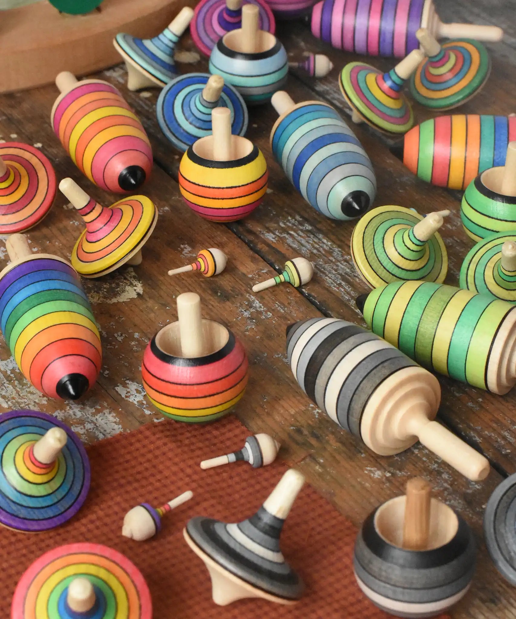Collection of Mader spinning top learning sets in different colour variations all laid out on a wooden surface in the Babipur playroom. 