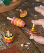 Mader fire spinning top learning set placed on a wooden surface in the Babipur playroom. One rallye spinner is shown in an adult's hand for scale.