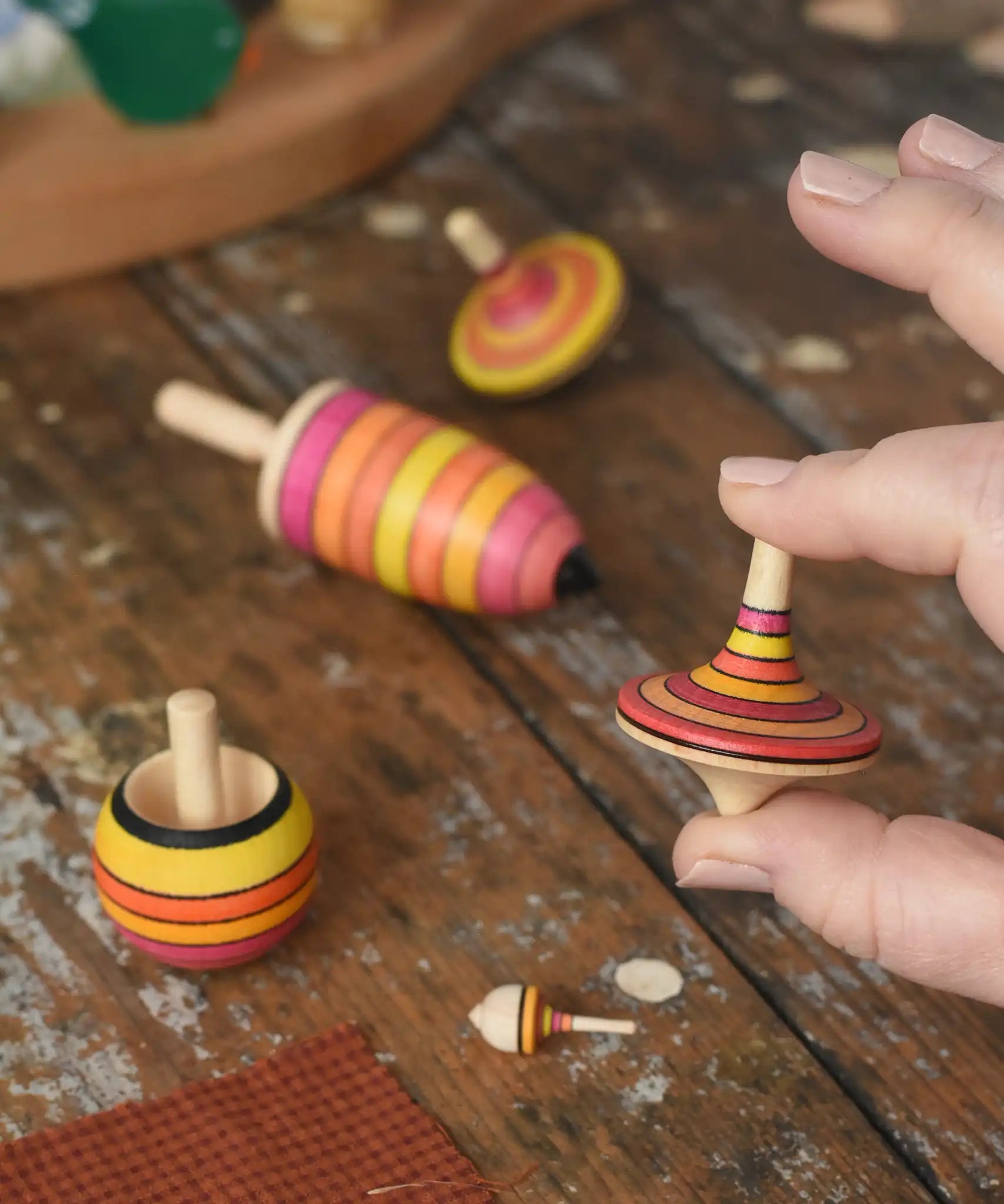Mader fire spinning top learning set placed on a wooden surface in the Babipur playroom. One rallye spinner is shown in an adult's hand for scale.