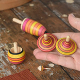 Mader fire spinning top learning set placed on a wooden surface in the Babipur playroom. Two rallye spinning tops shown in an adult's hand.