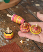 Mader fire spinning top learning set placed on a wooden surface in the Babipur playroom. Two rallye spinning tops shown in an adult's hand.