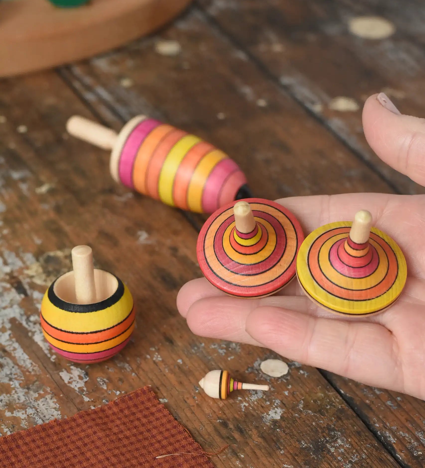 Mader fire spinning top learning set placed on a wooden surface in the Babipur playroom. Two rallye spinning tops shown in an adult's hand.