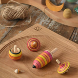 Mader fire spinning top learning set placed on an oak spinning plate on a wooden surface in the Babipur playroom.