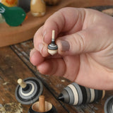 Miniature spinner from the Mader Kreiselmanufaktur graphite spinning top learning set in an adult's hand in the Babipur playroom. 