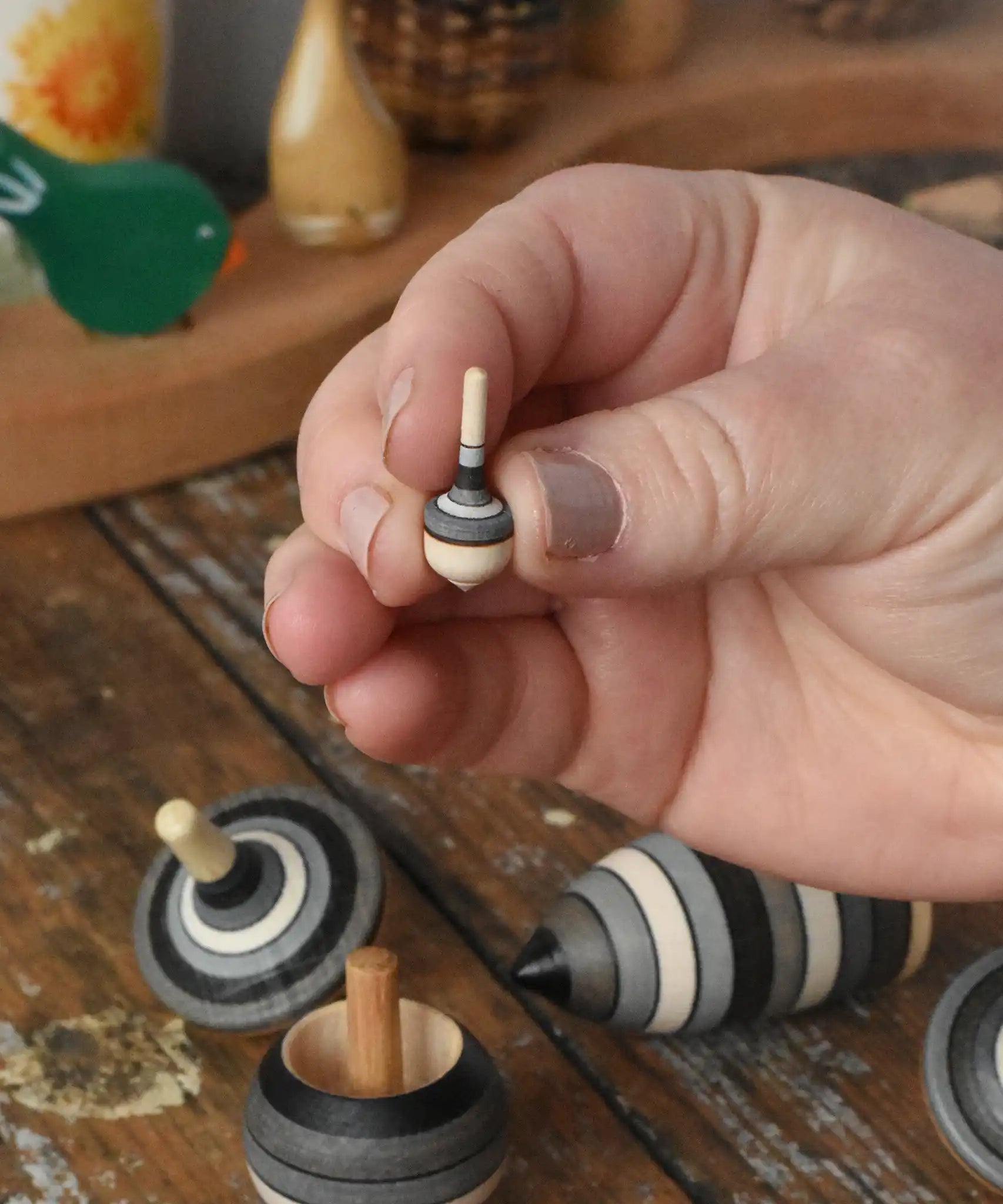 Miniature spinner from the Mader Kreiselmanufaktur graphite spinning top learning set in an adult's hand in the Babipur playroom. 