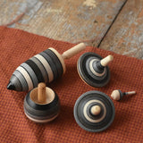 Mader Kreiselmanufaktur graphite spinning top learning set placed on a cloth on a wooden surface in the Babipur playroom. The set has 5 striped tops in shades of grey, white and black.