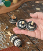 Rallye spinners from the Mader Kreiselmanufaktur graphite spinning top learning set in an adult's hand in the Babipur playroom. 