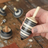 Thunderbolt spinner from the Mader Kreiselmanufaktur graphite spinning top learning set in an adult's hand in the Babipur playroom. 