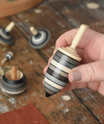 Thunderbolt spinner from the Mader Kreiselmanufaktur graphite spinning top learning set in an adult's hand in the Babipur playroom. 