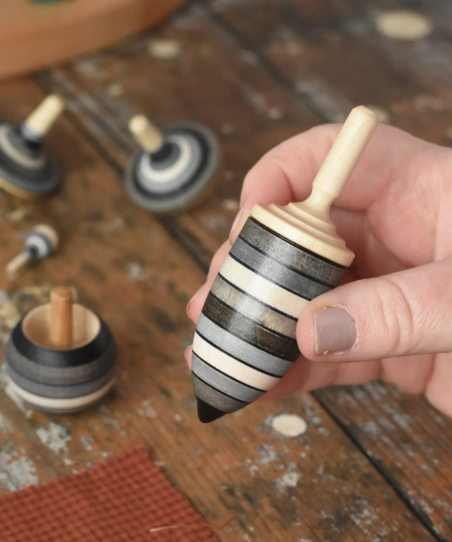Thunderbolt spinner from the Mader Kreiselmanufaktur graphite spinning top learning set in an adult's hand in the Babipur playroom. 