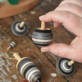 Turover top spinner from the Mader Kreiselmanufaktur graphite spinning top learning set in an adult's hand in the Babipur playroom. 
