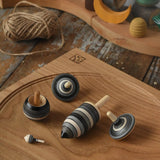 Mader Kreiselmanufaktur graphite spinning top learning set placed on an oak spinning plate on a wooden surface in the Babipur playroom. 