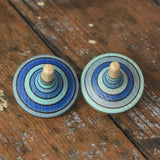 Two rallye spinners from the Mader Kreiselmanufaktur ice blue spinning top learning set on a wooden surface in the Babipur playroom. 