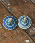 Two rallye spinners from the Mader Kreiselmanufaktur ice blue spinning top learning set on a wooden surface in the Babipur playroom. 