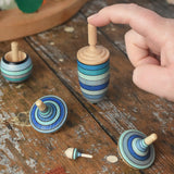 Mader Kreiselmanufaktur ice blue spinning top learning set on a wooden surface in the Babipur playroom. An adult's hand is holding up the thunderbolt spinner.