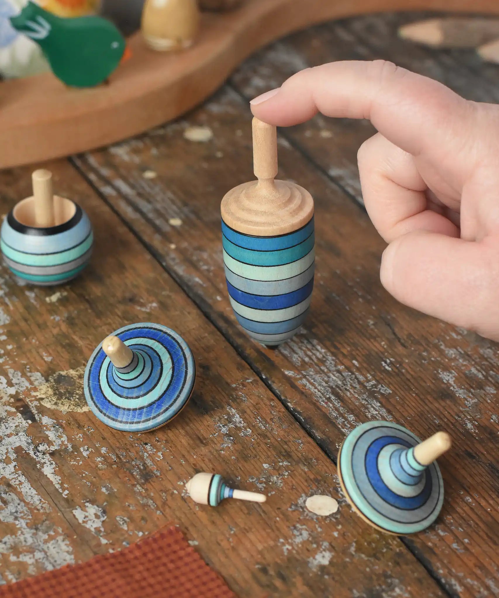 Mader Kreiselmanufaktur ice blue spinning top learning set on a wooden surface in the Babipur playroom. An adult's hand is holding up the thunderbolt spinner.