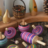 Mader lilac purple spinning top learning set placed on a wooden surface in the Babipur playroom. Grimm's celebration ring set up in the background.