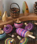 Mader lilac purple spinning top learning set placed on a wooden surface in the Babipur playroom. Grimm's celebration ring set up in the background.