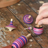 Mader lilac purple spinning top learning set placed on a wooden surface in the Babipur playroom. An adult's hand can be seen picking up the turnover top