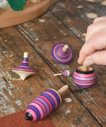 Mader lilac purple spinning top learning set placed on a wooden surface in the Babipur playroom. An adult's hand can be seen picking up the turnover top