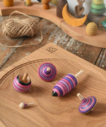Mader lilac purple spinning top learning set placed on an oak spinning plate on a wooden surface in the Babipur playroom. 