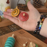 The red and yellow spinning tops from the Mader Kreiselmanufaktur multicolour spinning top learning set in an adult's hand in the Babipur playroom. 