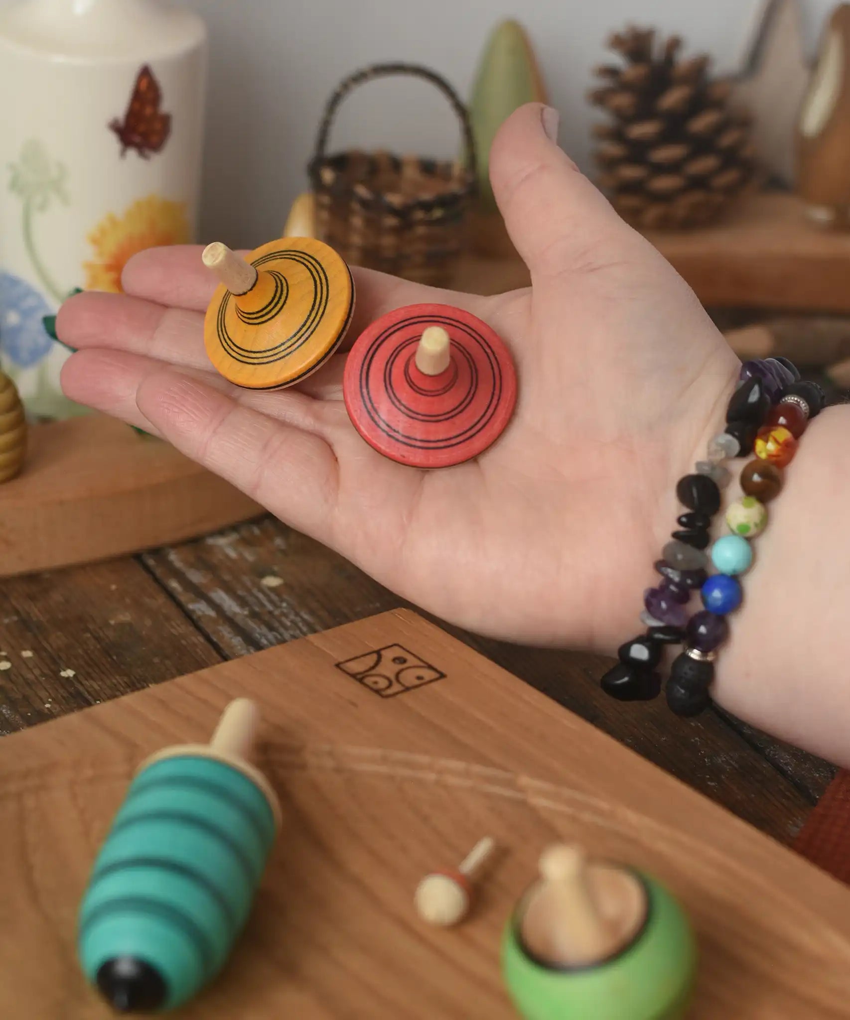 The red and yellow spinning tops from the Mader Kreiselmanufaktur multicolour spinning top learning set in an adult's hand in the Babipur playroom. 
